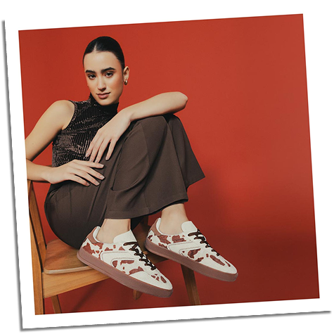 Modelo sentada sobre silla usando  tenis estampados café y blanco, look urbano moderno de la marca ela, ultima colección