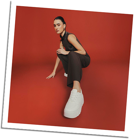 Mujer con tenis blancos de plataforma y outfit marrón sobre fondo rojo, estilo casual chic de la ultima colección de ela