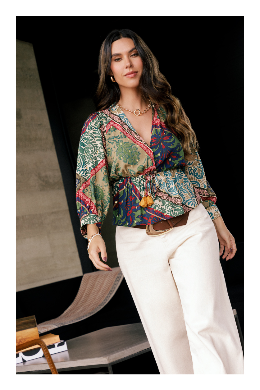 Modelo Daniela Salazar vistiendo blusa holgada de mangas largas estampada, cinturón café, pantalón blanco y accesorios.