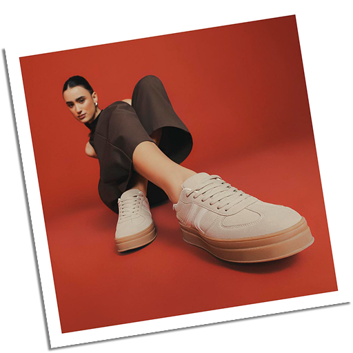 Modelo con tenis beige y suela alta, outfit marrón elegante sobre fondo rojo.