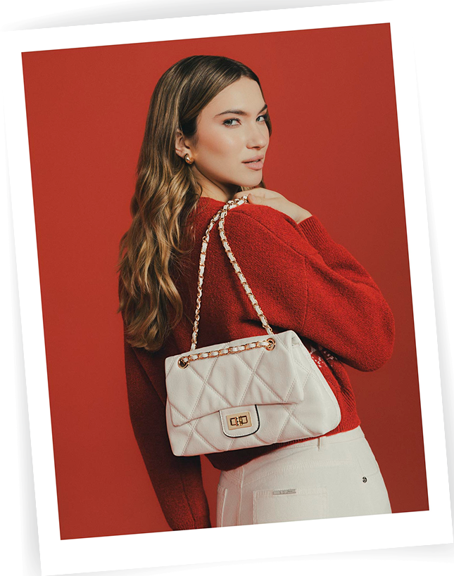 Modelo con suéter rojo de espalda sosteniendo un bolso blanco acolchado, look femenino elegante de la última colección de la marca ela