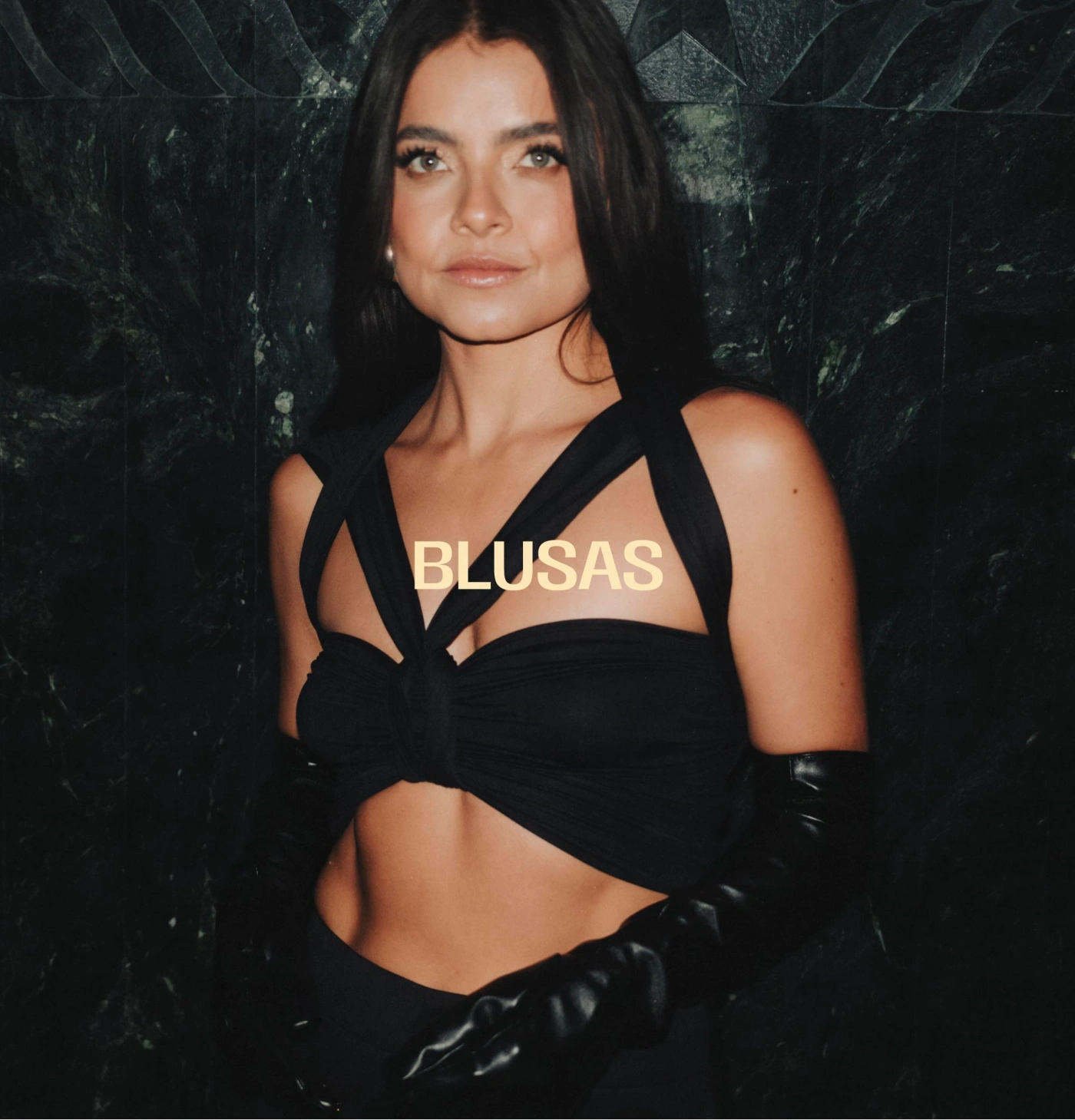 Mujer con blusa crop negra de aberturas, pantalón negro y guantes largos.
