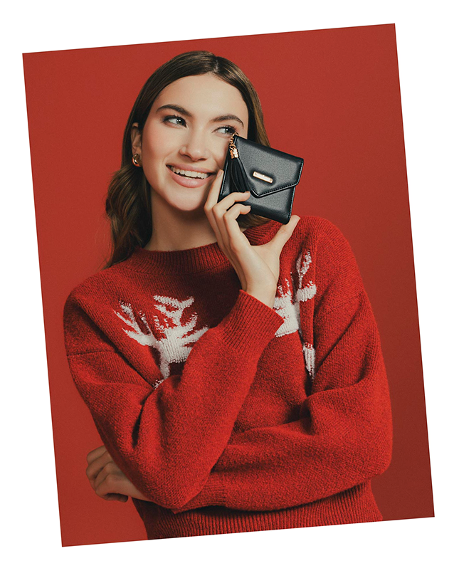 Mujer con suéter rojo navideño sostiene una billetera negra pequeña, estilo moderno y femenino de la marca ela
