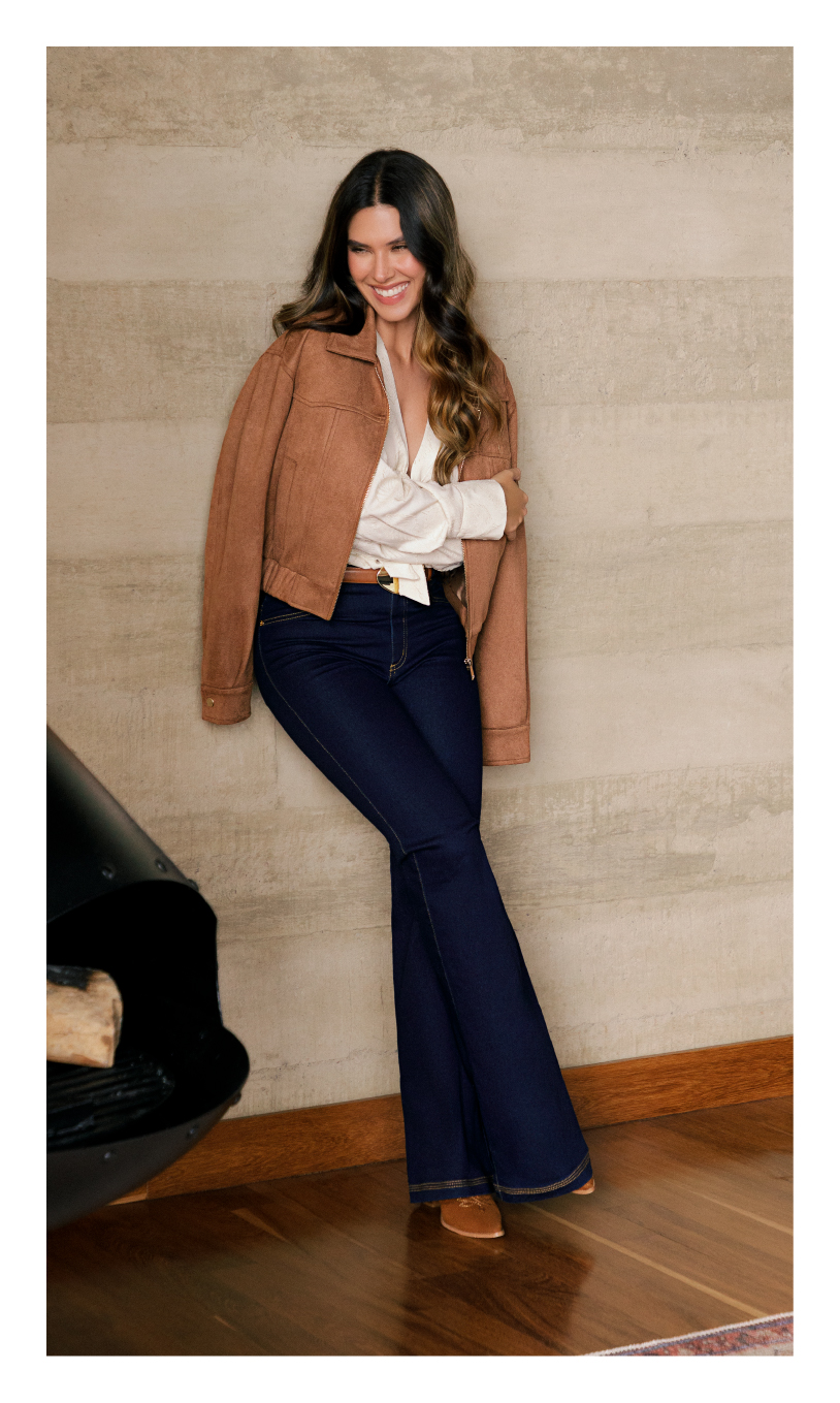 Foto de modelo usando jeans mujer, chaqueta café y camisa blanca de fondo de la marca ELA
